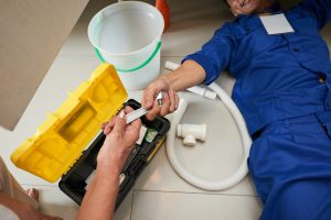 Senior woman passing wrench to plumber who is lying on the floor